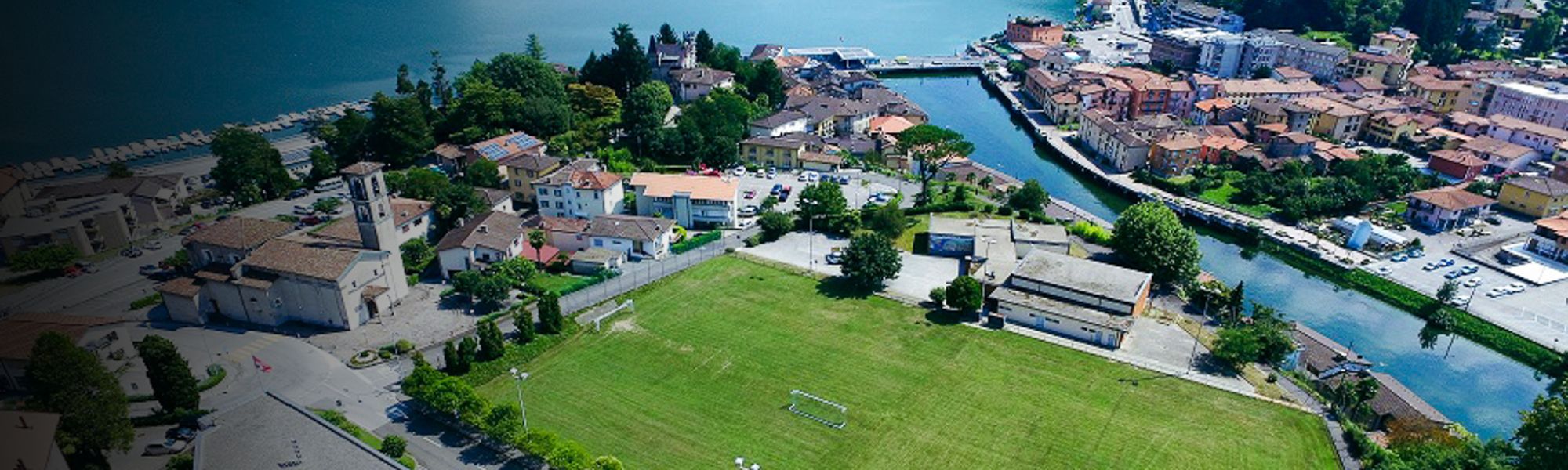 Fu&szlig;ballplatz in der Schweiz, umgeben von H&auml;usern und einem Fluss, mit Blick auf den See.