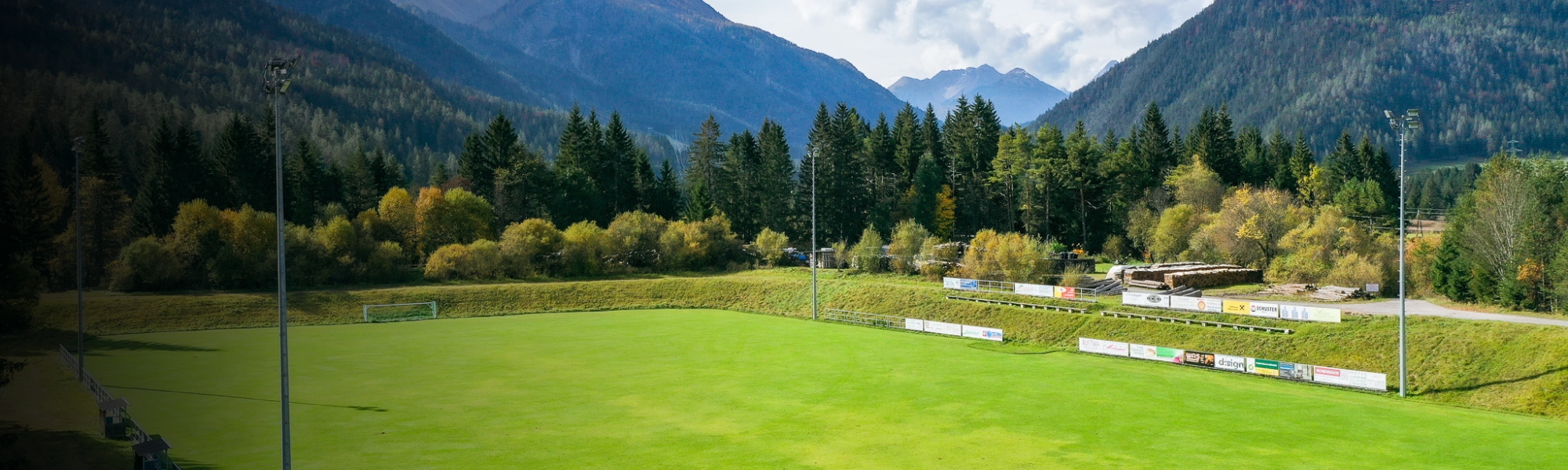 Fu&szlig;ballplatz in idyllischer Berglandschaft in Tirol, mit Blick auf W&auml;lder und die Alpen im Hintergrund.